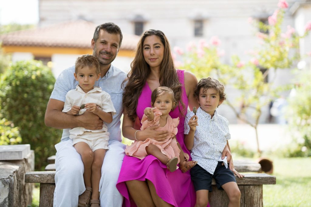 Dawn Lioutas sitting with her husband, 2 sons and 1 daughter together on a bench in a garden.