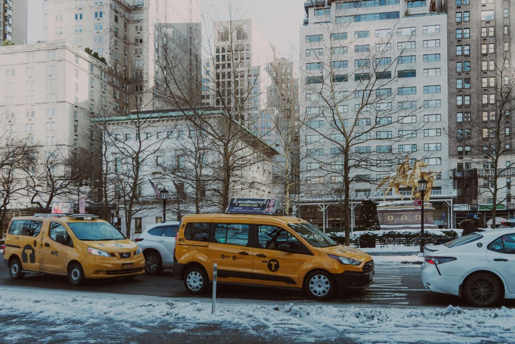 Yellow NYC taxis driving past snowy Central Park with city buildings in background