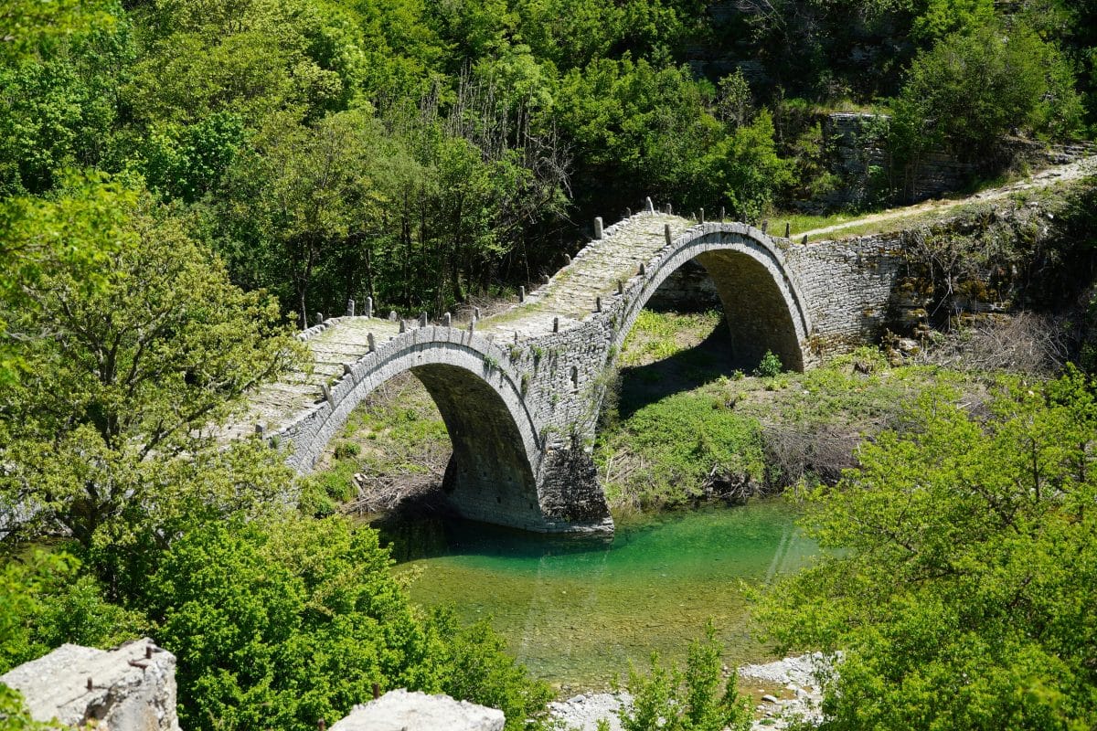 Kokkoris stone bridge over the Voidomatis River in Zagori, Epirus Greece surrounded by lush green forest