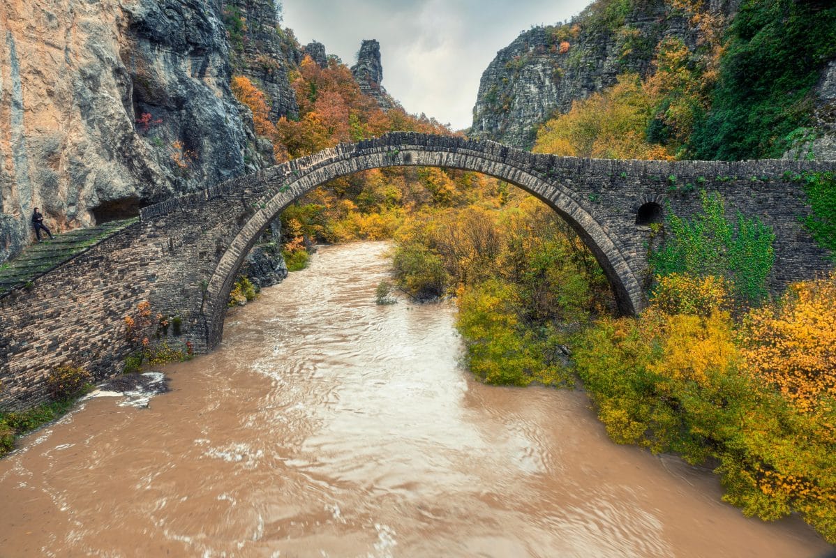 Plakida or Kokkori stone bridge over the Voidomatis River in Zagori, Epirus Greece surrounded by autumn mountains