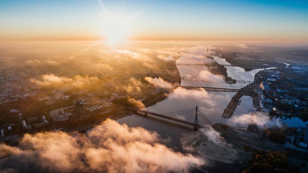 Aerial view of Riga Latvia at sunrise with the Daugava River, bridges, and city skyline above morning clouds