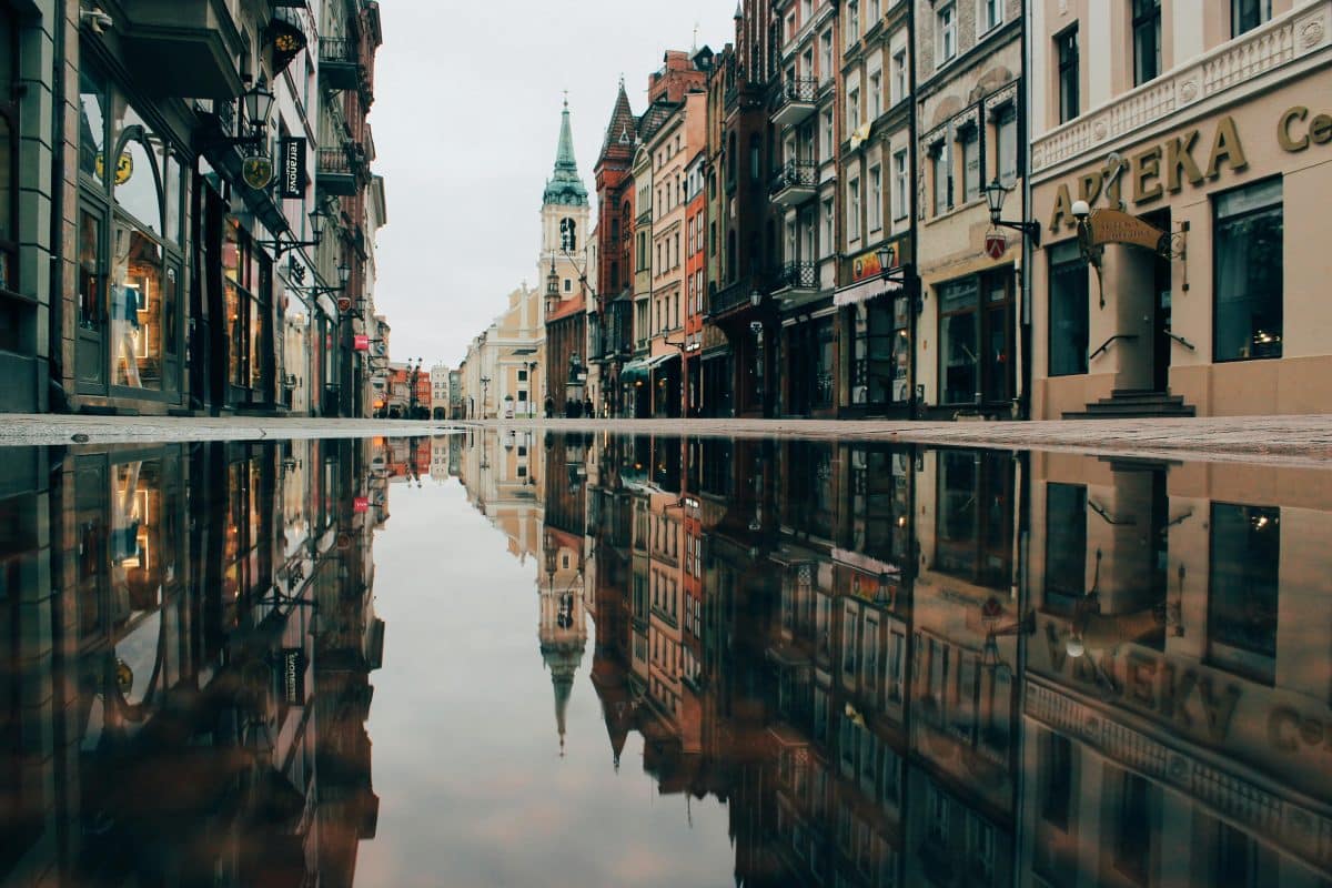 Historic street in Old Town Toruń Poland with colorful buildings and church tower reflected in a puddle