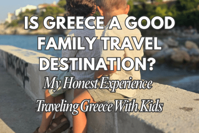 Two young children sit side by side on a stone wall overlooking the sea in Greece, enjoying a calm coastal view during a family trip.