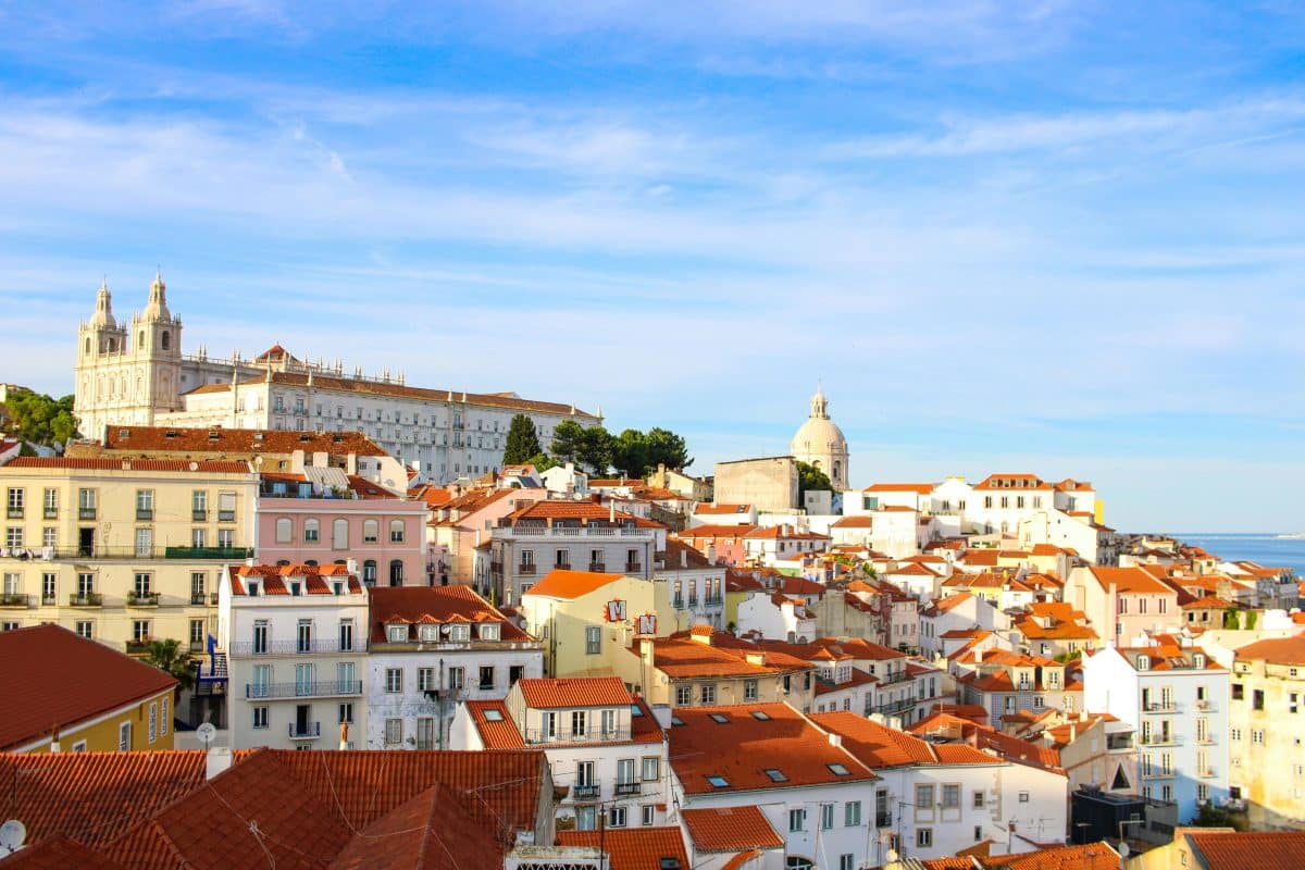 View over Alfama Lisbon with red rooftops and historic buildings under blue sky