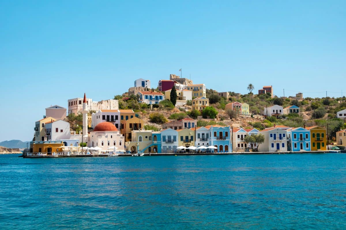 Colorful houses lining the harbor of Kastellorizo island in Greece overlooking turquoise Mediterranean water.