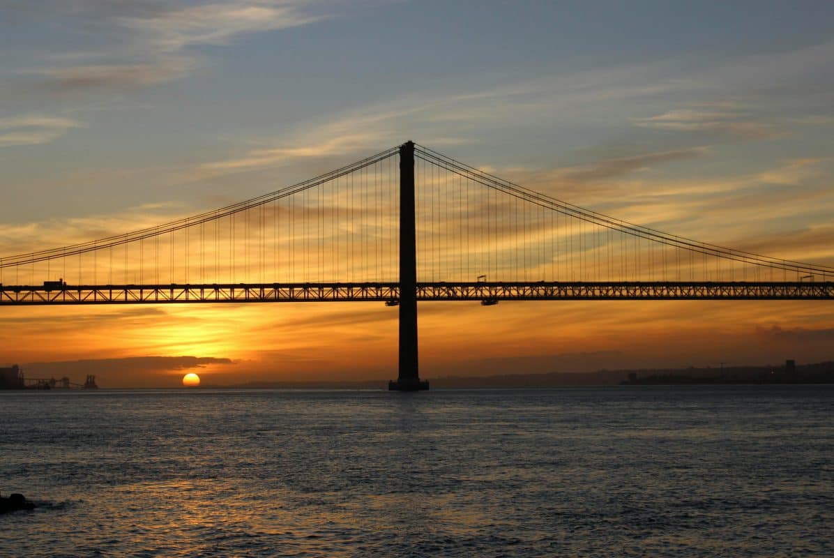 sunset over 25 de abril bridge in lisbon with tagus river