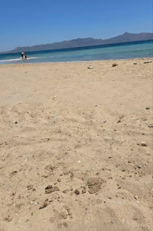 Sandy Skala Beach in Agkistri Greece with shallow clear water and mountains in the distance