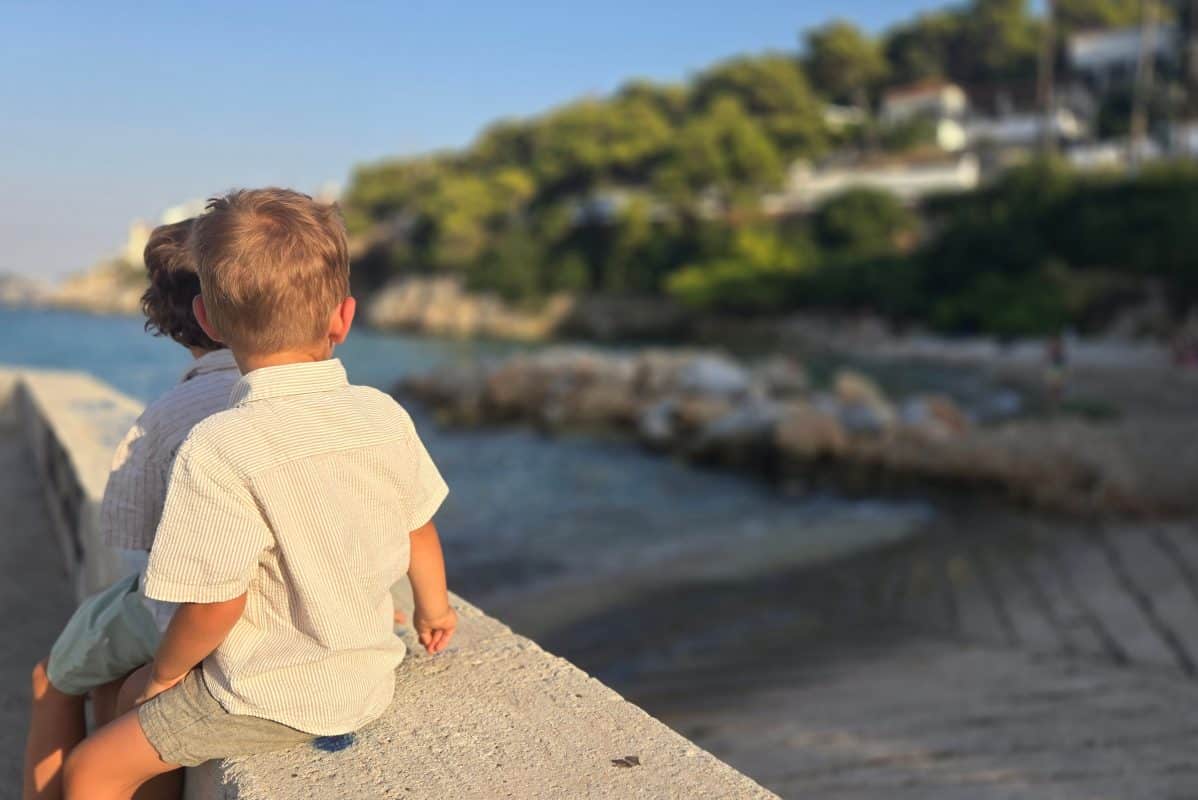 Two young children sitting by the waterfront in Agistri, Greece, overlooking the sea during a family vacation.
