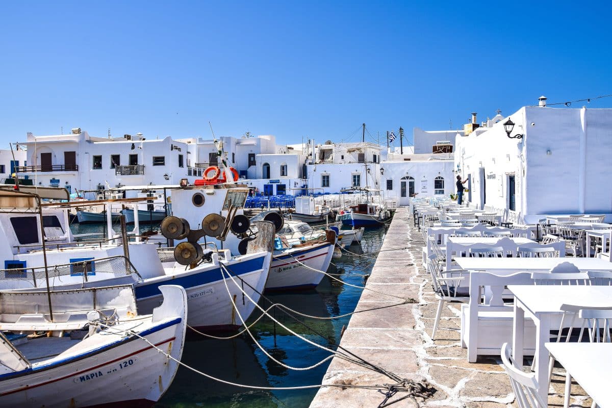 Fishing boats docked in Naoussa Harbor in Paros, Greece, with whitewashed buildings and waterfront restaurants lining the marina.