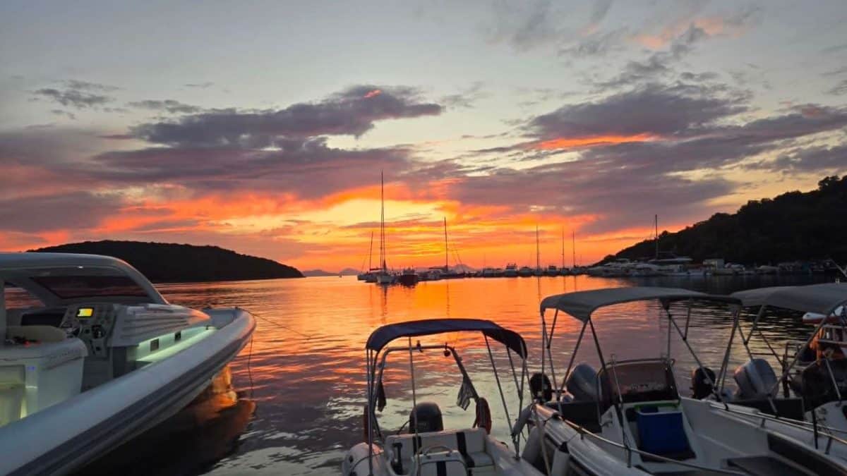 Boats docked in Syvota Marina at sunset with colorful skies reflected on the water.