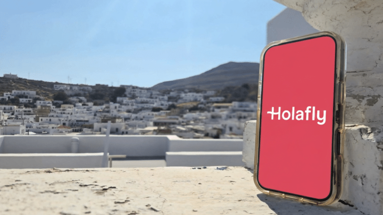 Phone displaying the Holafly eSIM app overlooking the whitewashed village of Lindos in Rhodes, Greece.