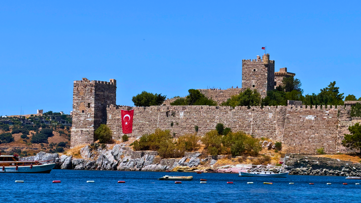 Bodrum Castle overlooking the turquoise water of Bodrum Harbour in Turkey, with historic stone walls and Turkish flags.