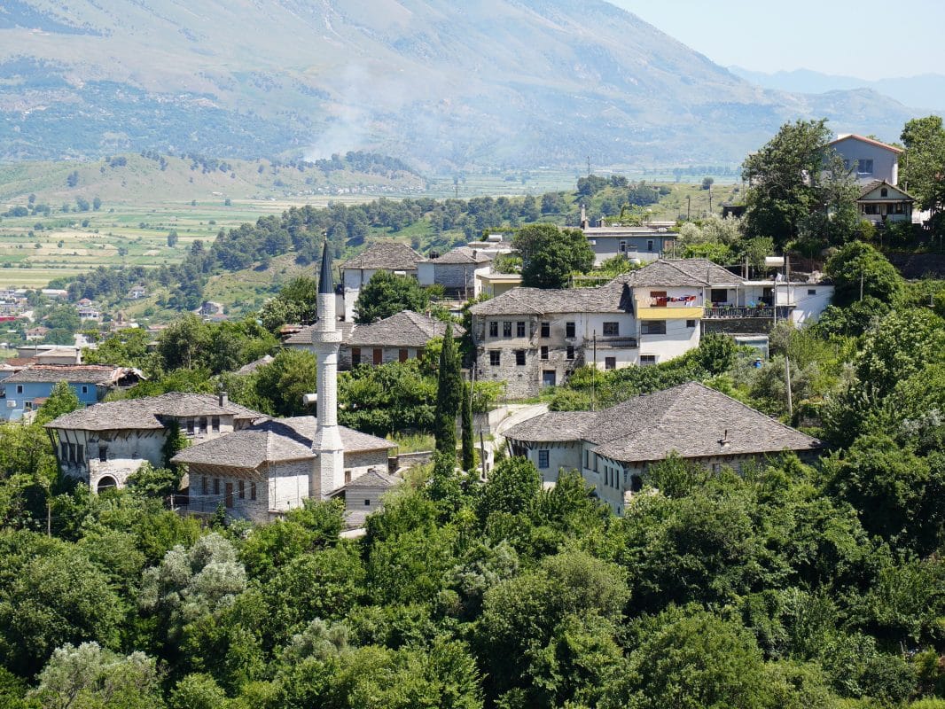 Traditional stone-roofed houses and a mosque in Gjirokastër, Albania, surrounded by green hills.