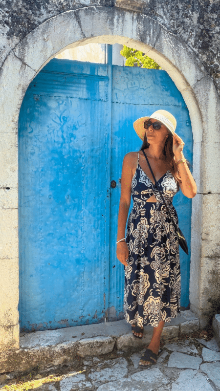 Woman standing in front of a blue arched door in Himarë Old Town, Albania