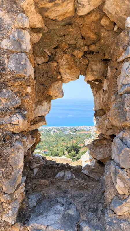View of the Ionian Sea and coastline through an old stone window in Himarë Old Town, Albania